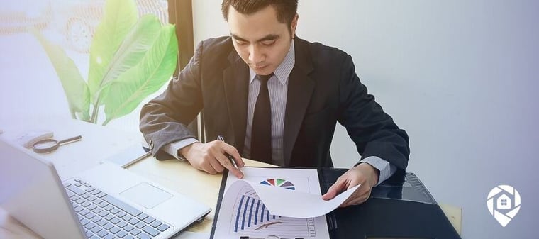 Young real estate investor reviewing property deal reports at desk — real estate wholesaling and house flipping business strategy.