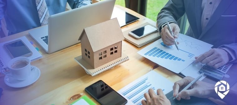 Real estate investors discussing seller financing strategies with property model and financial charts.