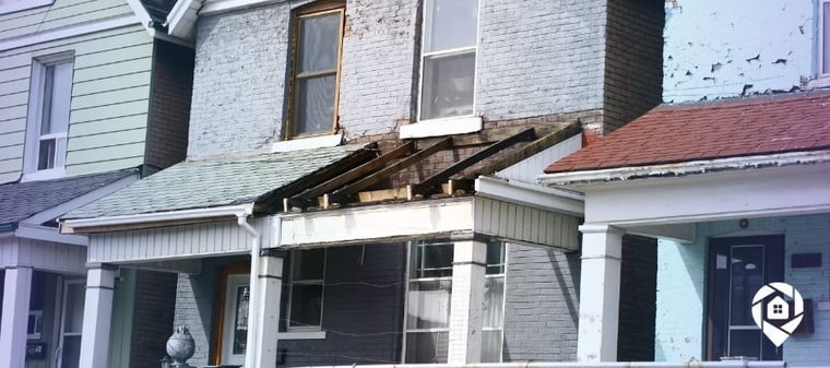 Distressed two-story house with damaged porch—ideal for real estate flipping and investment.